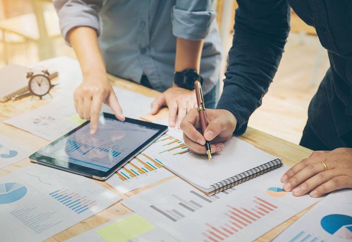 Startup Concept.Young businessman holding pen Writing a summary report on a notebook and A friend pointing on tablet to explain the work plan at home office.