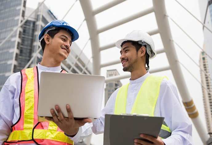 Two Handsome smile Burmese or Myanmar engineer manager and electrician using computer laptop to check construction project plan progress in Bangkok Modern city. Industrial concept.